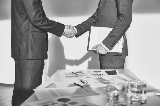 Two businessmen in formalwear handshaking after signing contract